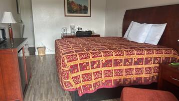 Une chambre d’hôtel avec un grand lit, une table de chevet en bois, un bureau avec une lampe et un tableau au mur.