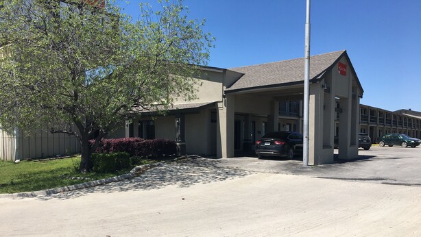 A building with a covered parking area, a tree, and a clear blue sky. - Quest Inn (Weatherford)
