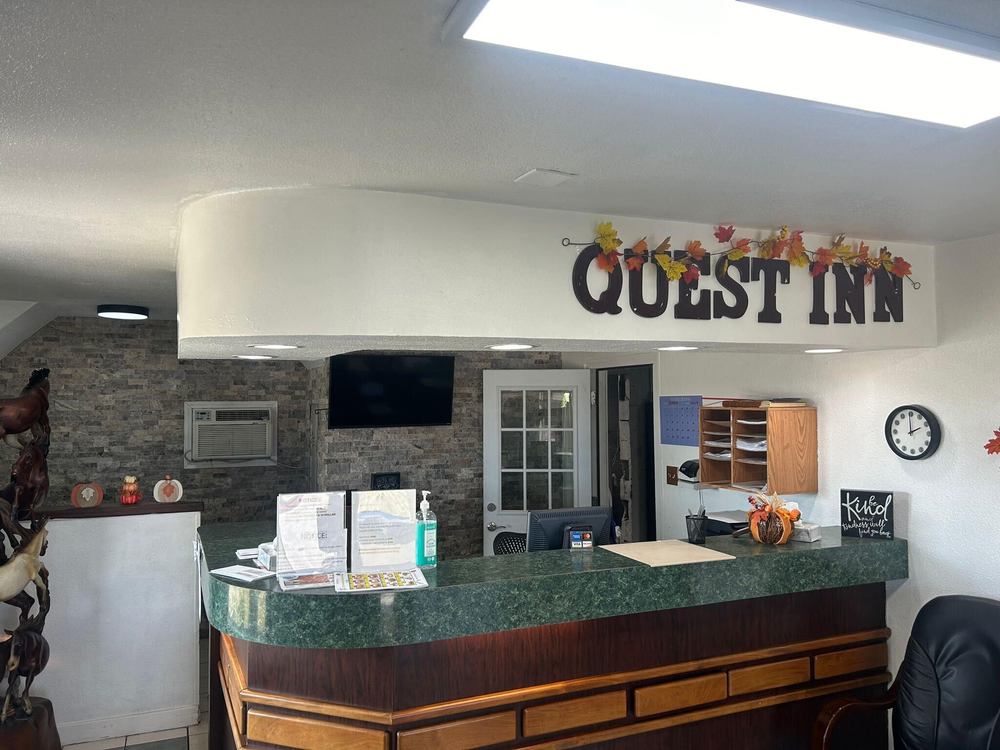 A reception area with a stone wall, a flat-screen TV, a wooden counter, and a sign that reads "QUEST INN".