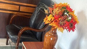 A seating area with two black leather chairs, a wooden table, and a vase with a floral arrangement. - Quest Inn (Weatherford)