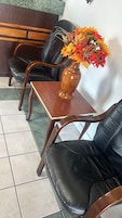 Un rincón de descanso con dos sillones de cuero negro, una mesa de madera y un florero con arreglos florales.