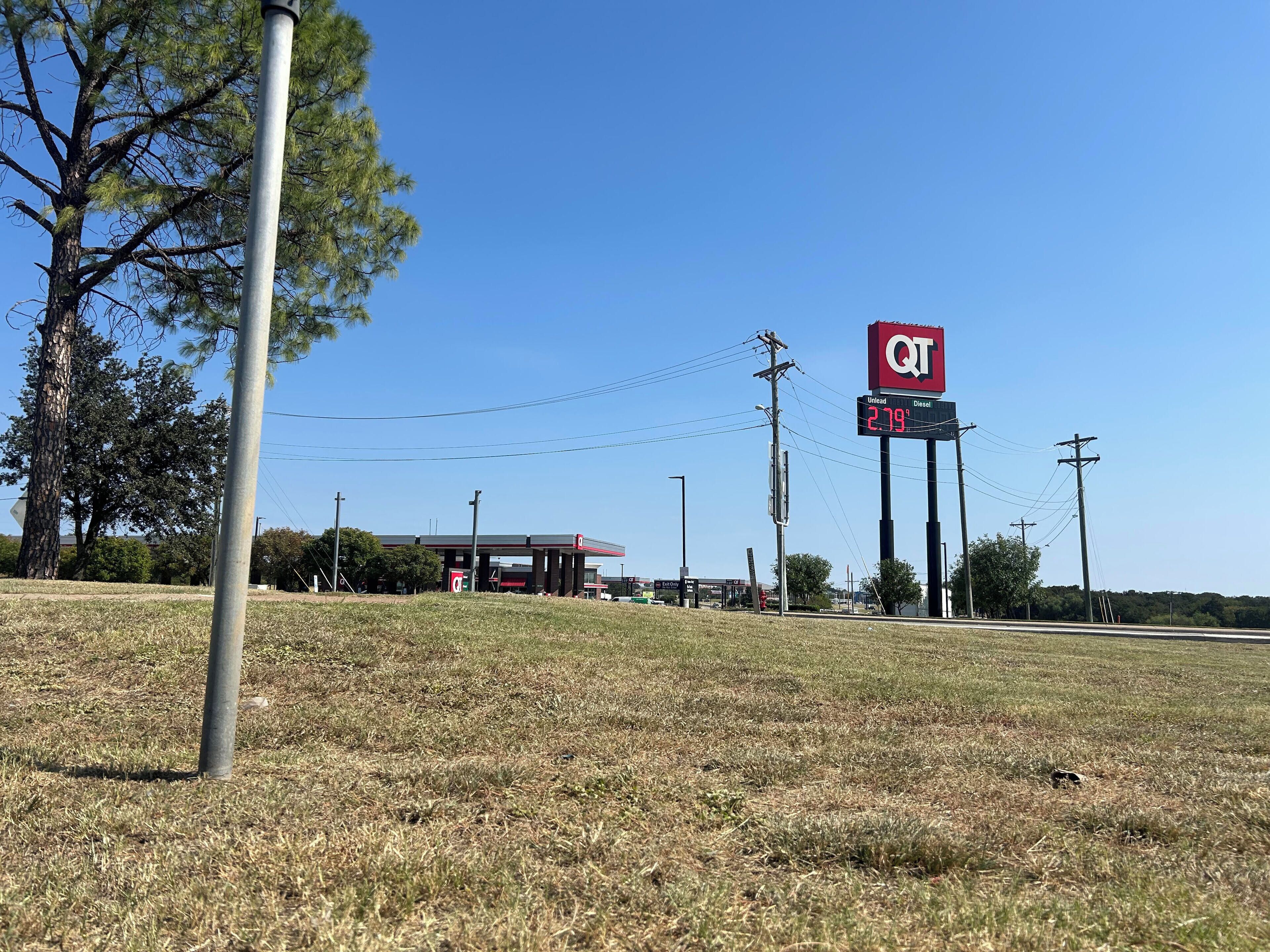 Une station-service avec un ciel dégagé, une enseigne QT rouge et un champ d’herbe.