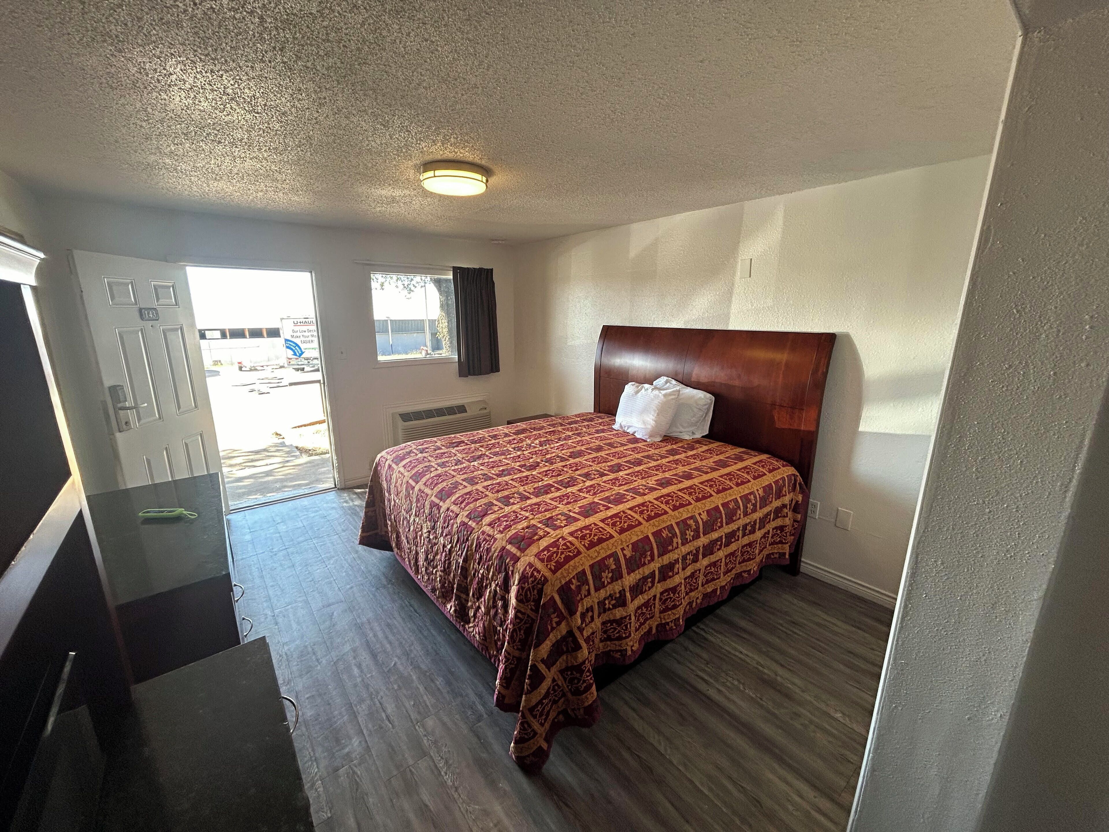 Una habitación de hotel con cabecera de madera, una colcha estampada y una puerta con el letrero de U-Haul.