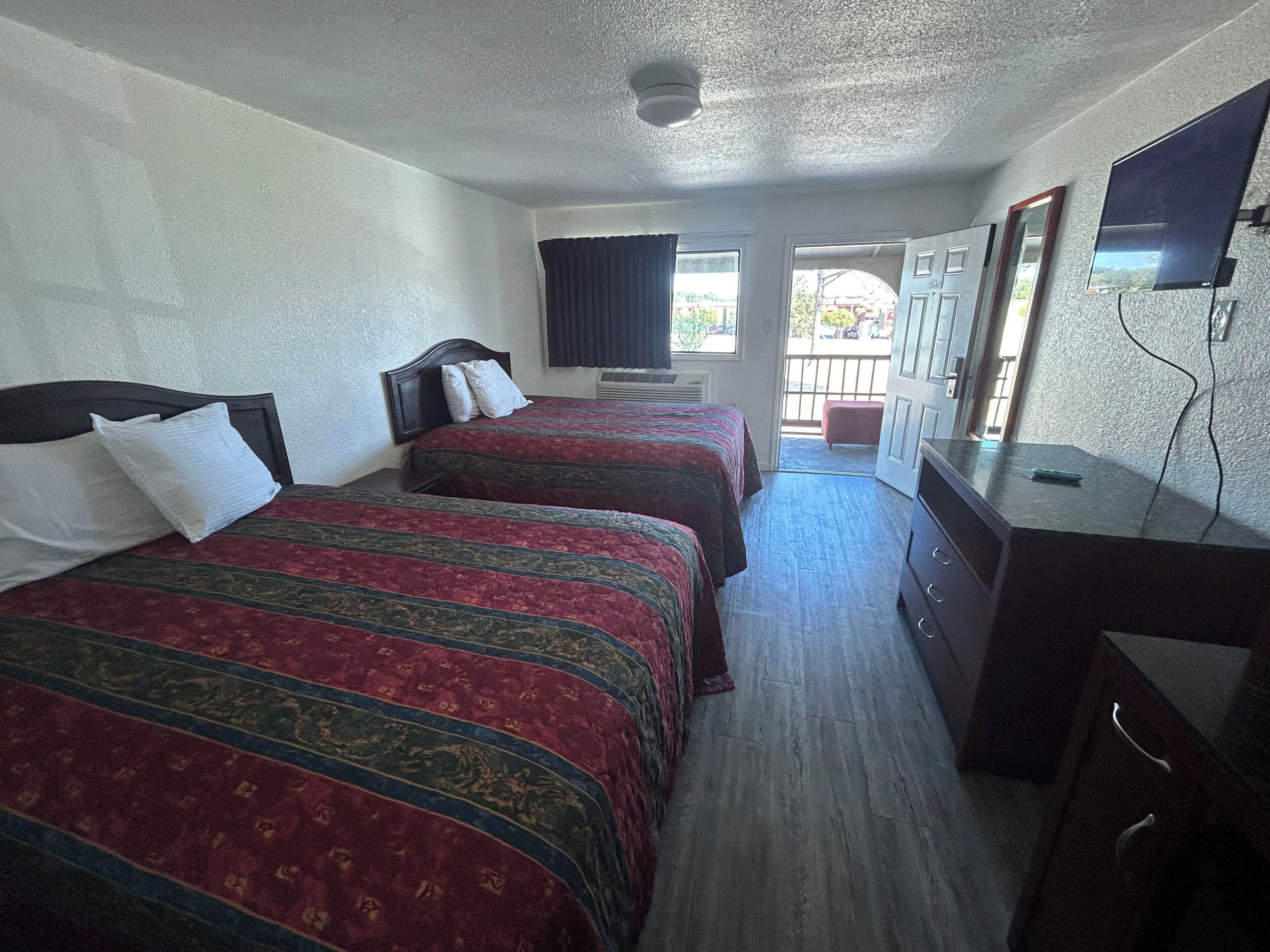 A hotel room with two beds, a TV, a dresser, and a balcony.