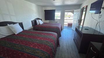 A hotel room with two beds, a TV, a dresser, and a balcony.