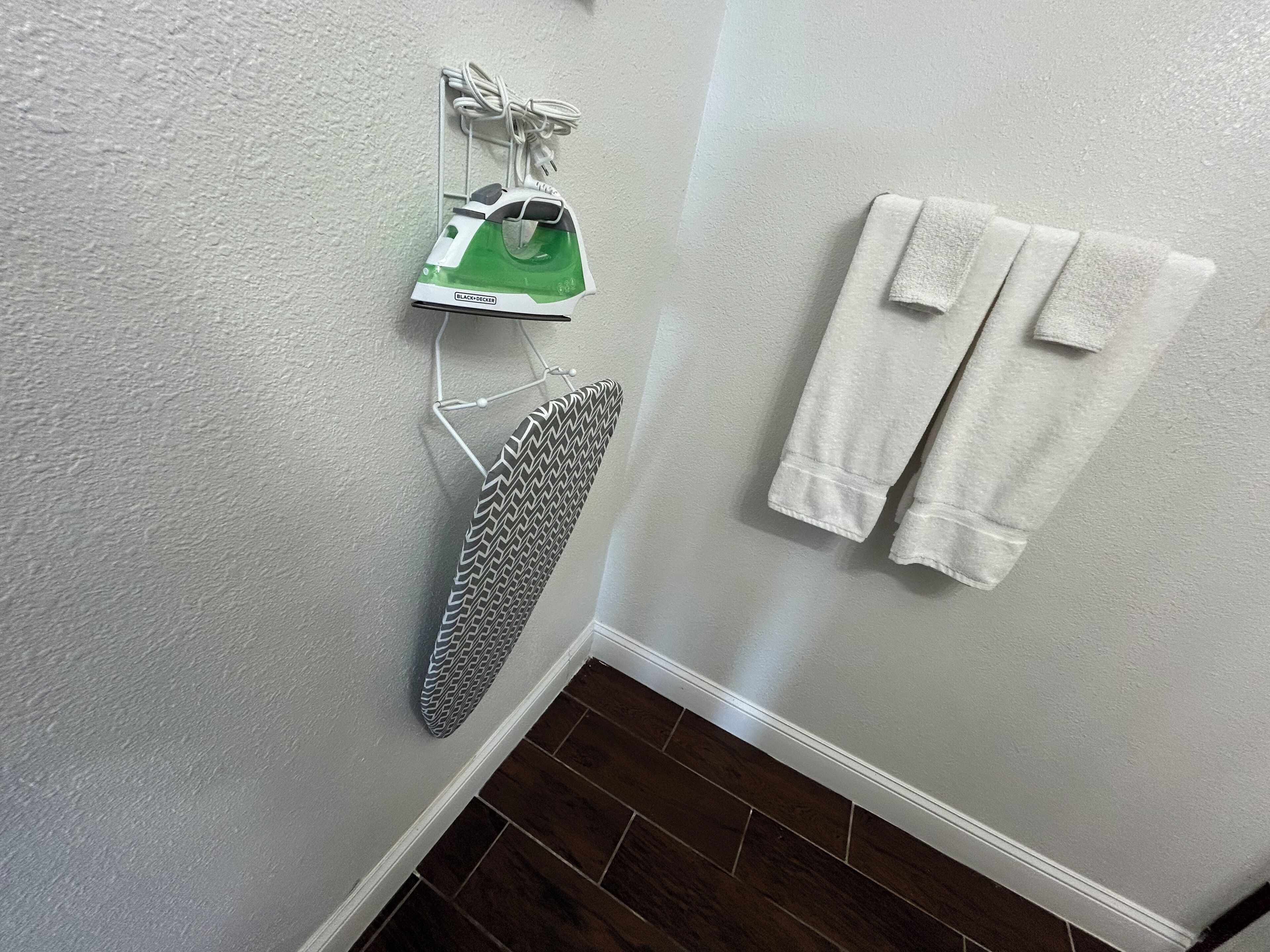 Une salle de bain avec un mur blanc, un plancher en bois, un fer à repasser et deux serviettes suspendues à un porte-serviettes.