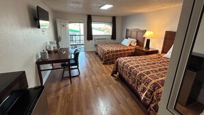 A hotel room with two beds, a desk, a chair, a TV, and a window with a view. - Quest Inn (Weatherford)