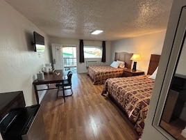 Habitación de hotel con dos camas, un escritorio, una silla, un televisor y una ventana con vistas.