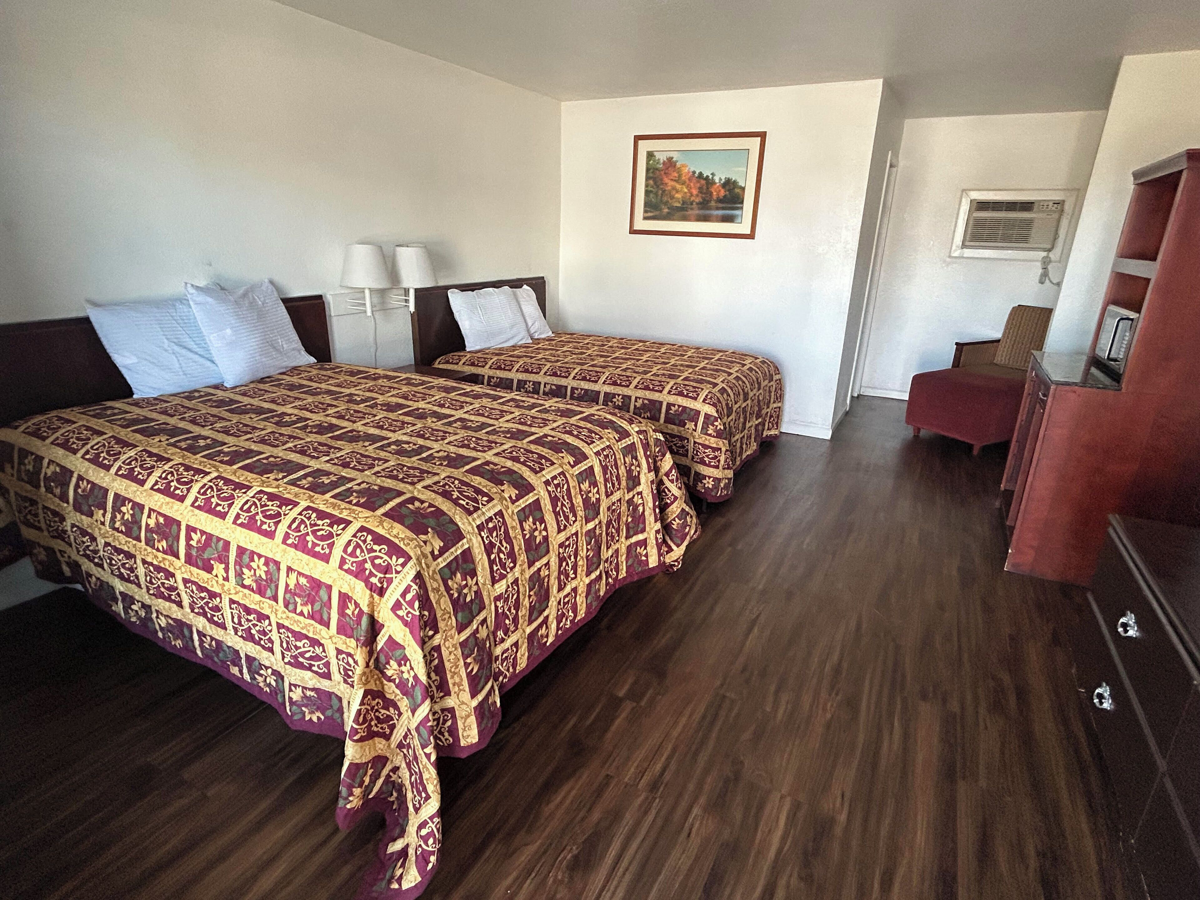 A hotel room with two beds, a desk, a chair, and a painting on the wall.