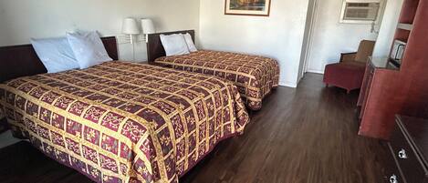 A hotel room with two beds, a desk, a chair, and a painting on the wall.