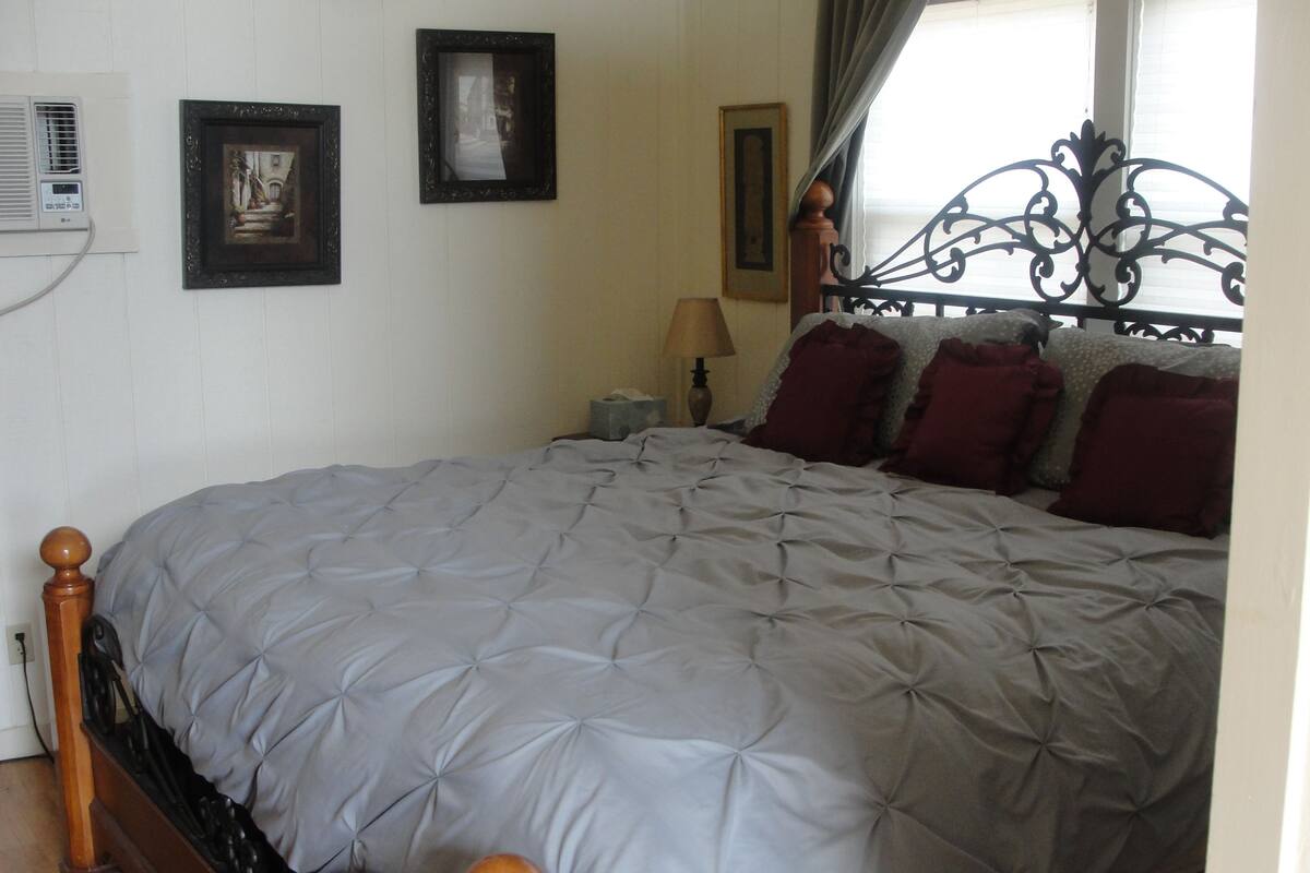 A neatly made bed with a grey quilt, a wooden headboard, and a bedside table with a lamp.