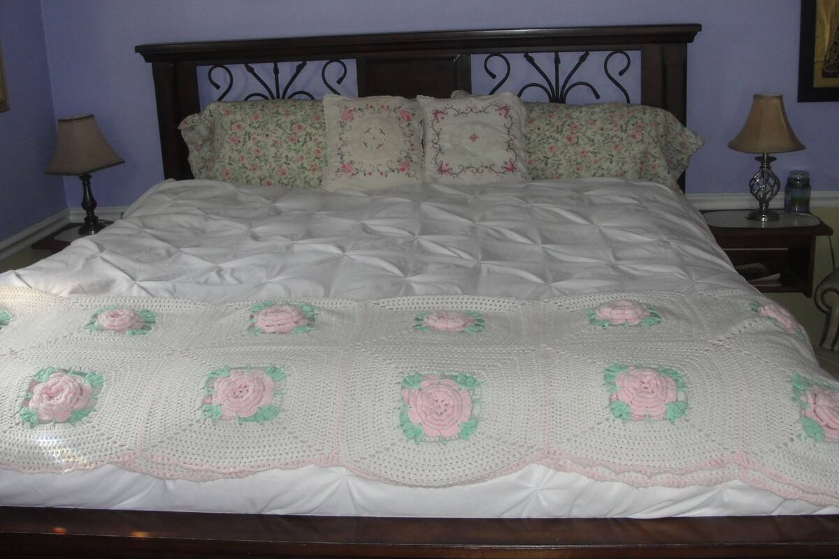 A neatly made bed with a floral-patterned quilt and pillows, a wooden headboard, and framed pictures on the wall.