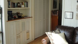 A living room with a brown leather sofa, a bookshelf, a white closet with louvered doors, and a small table with a bowl and books. - Stone Meadow Resort (Eureka Springs)