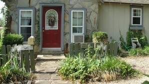 A stone house with a red door, two windows, and a stone pathway leading to the entrance. - Stone Meadow Resort (Eureka Springs)