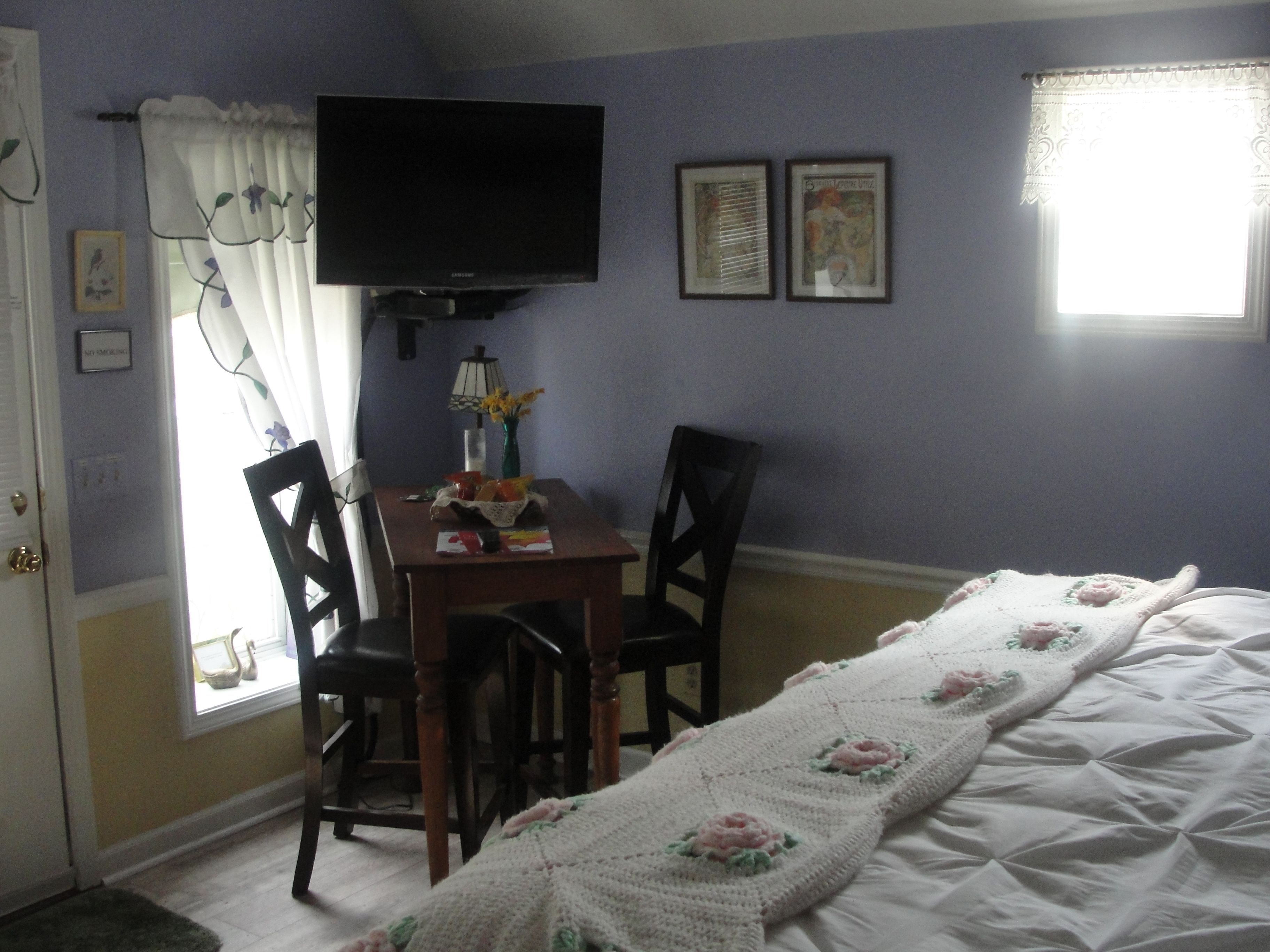 Un dormitorio con una cama, un escritorio con sillas, un televisor y dos cuadros en la pared.