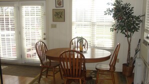 A dining area with a round wooden table, four chairs, a potted plant, and a window with blinds. - Stone Meadow Resort (Eureka Springs)