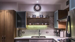 A modern kitchen with wooden cabinets, a stainless steel refrigerator, a built-in oven, and a coffee maker on the countertop. - Casa Iguana at Carranza (Puerto Vallarta)