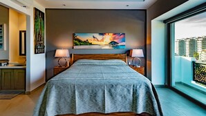 A modern bedroom with a large bed, a painting of a sunset, and a balcony with a view of buildings. - Casa Iguana at Carranza (Puerto Vallarta)