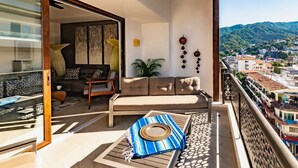 A balcony with a sofa, a patterned rug, and a view of a cityscape with mountains. - Casa Iguana at Carranza (Puerto Vallarta)