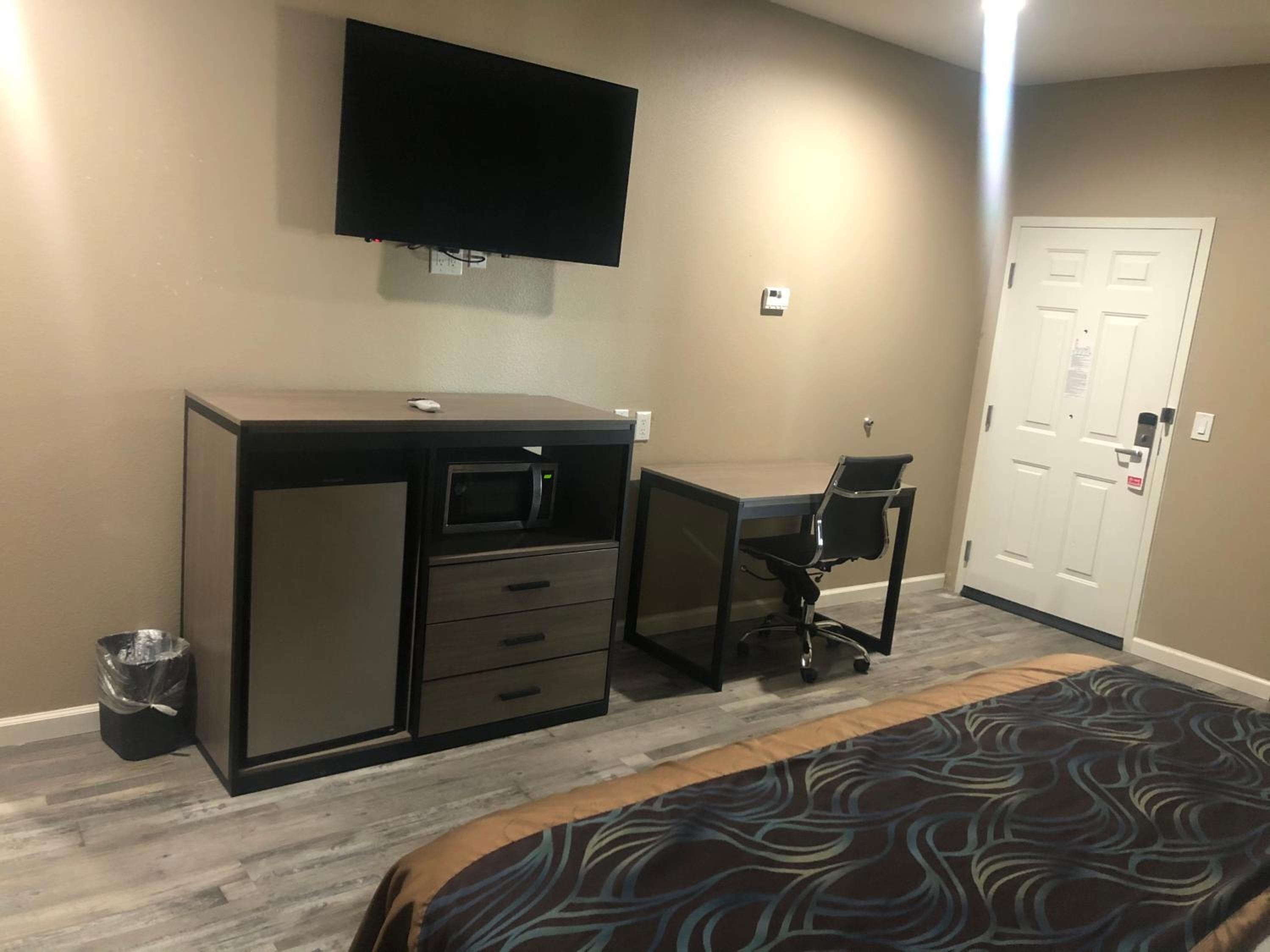 Una habitación de hotel con cama, escritorio con computadora, televisor en la pared y una puerta.