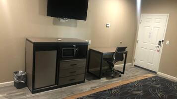 Una habitación de hotel con cama, escritorio con computadora, televisor en la pared y una puerta.