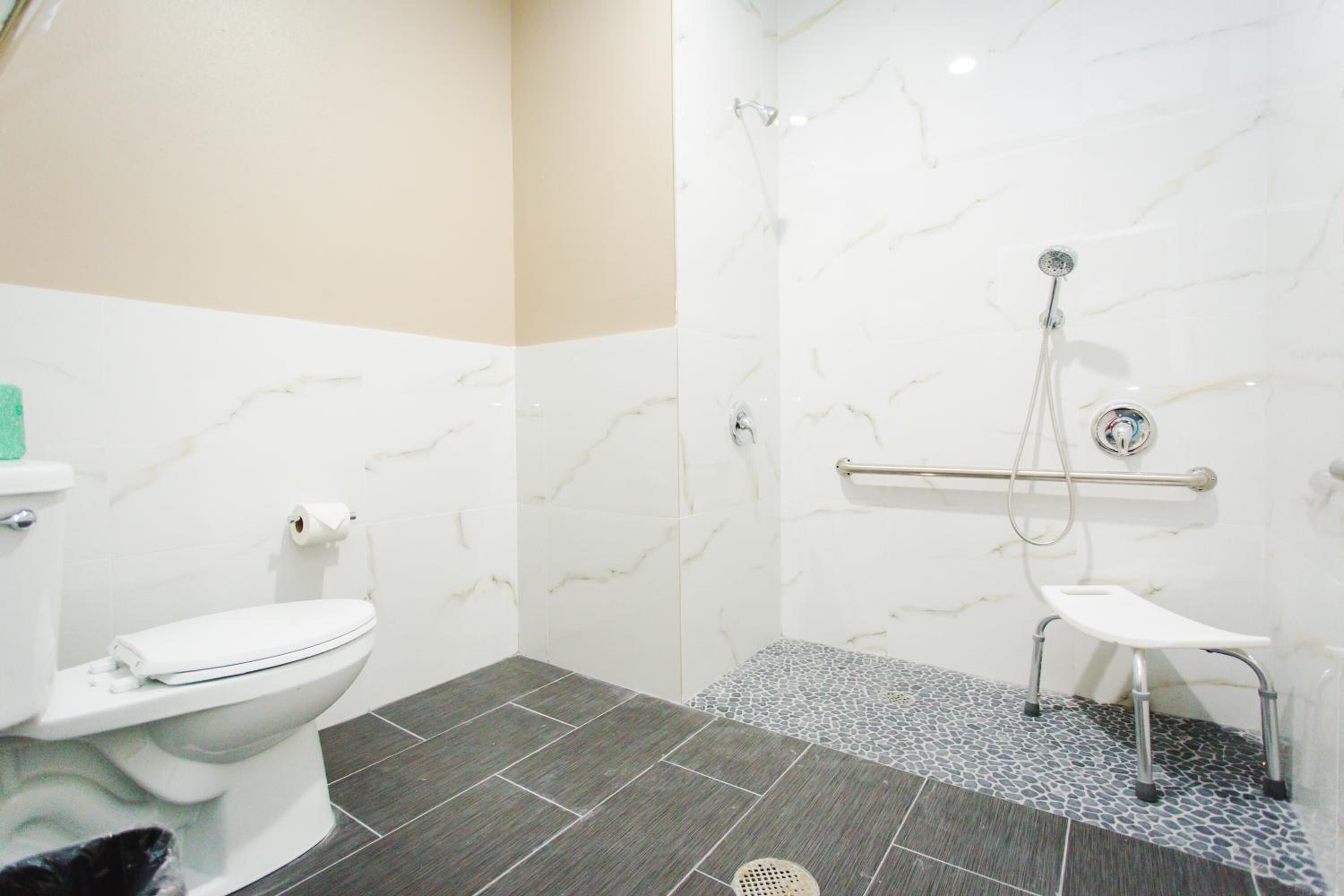 A bathroom with a toilet, a shower with a grab bar, and a small bench.