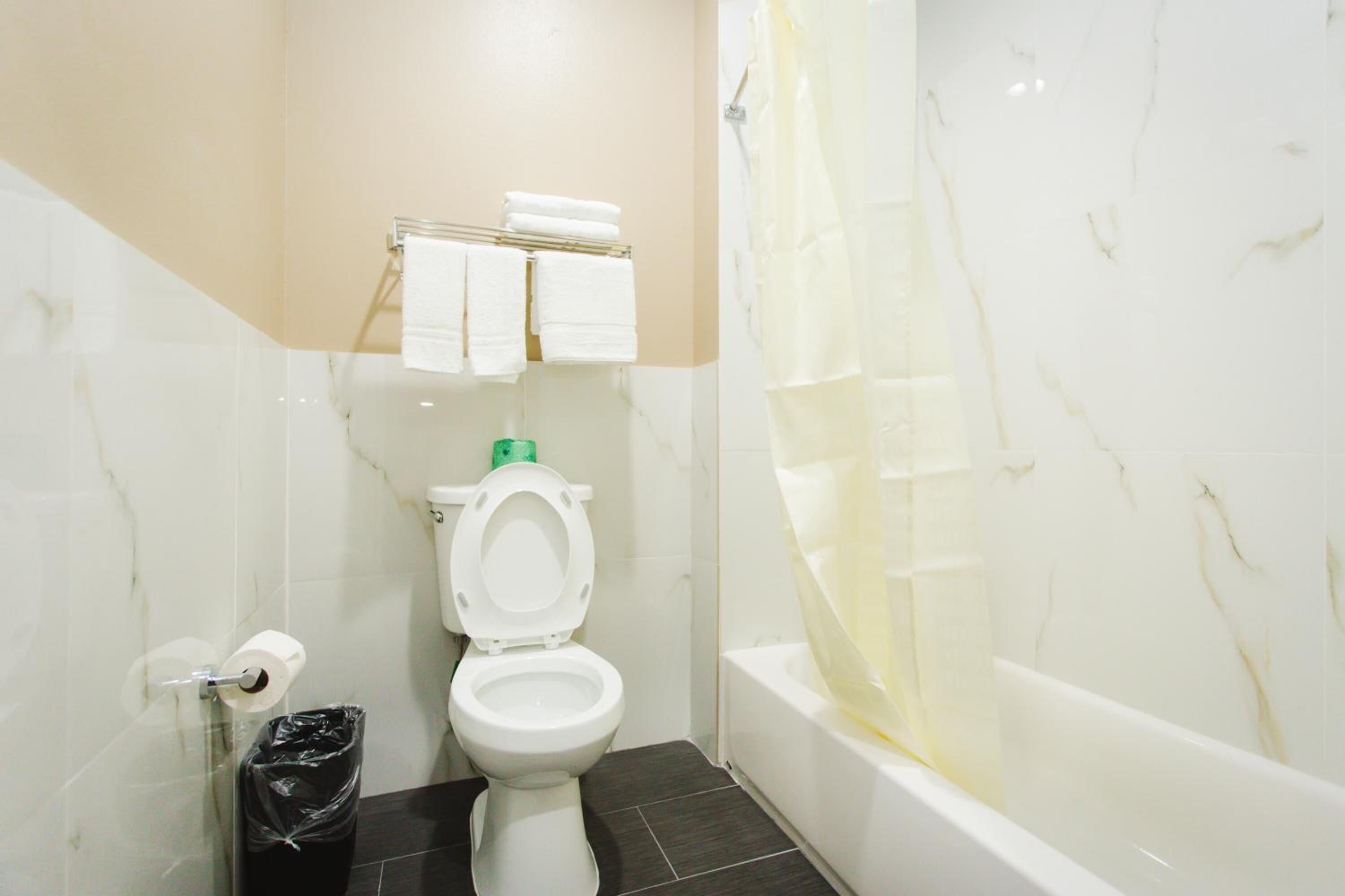 A bathroom with a toilet, a trash bin, a towel rack with towels, and a bathtub.