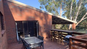 Un espace patio doté d’une porte vitrée donnant sur un espace extérieur abrité, une terrasse en bois et une table avec des chaises.