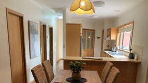 Un coin repas avec une table et des chaises en bois, un luminaire suspendu et une cuisine en arrière-plan.