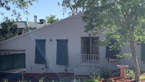 Une maison moderne à deux étages, dotée d’un toit plat, d’un porche avant couvert et d’un petit jardin agrémenté de paillis et de plantes.