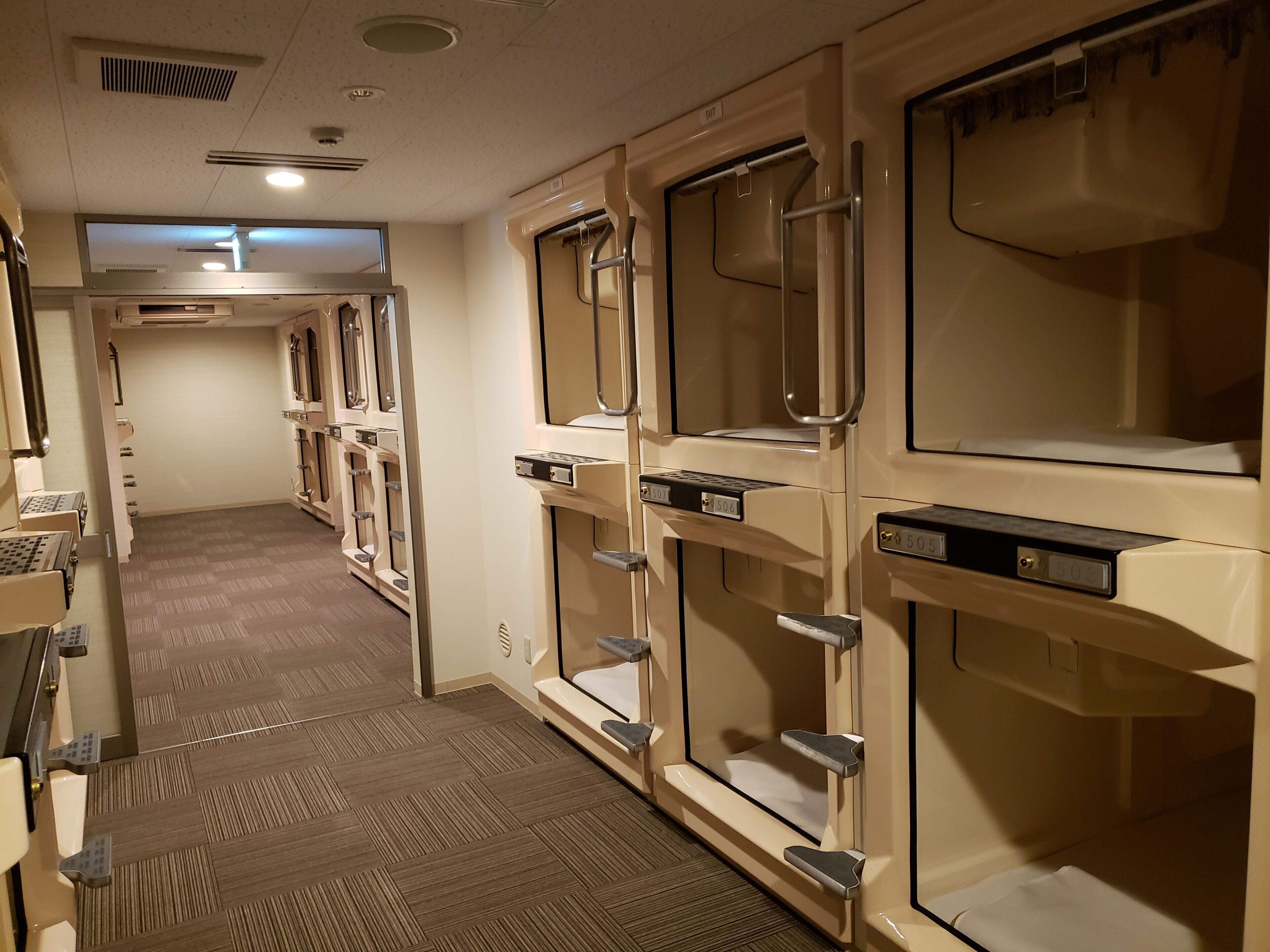A hotel corridor with rows of ensuite bathrooms, each with a vanity, mirror, and towel rack.