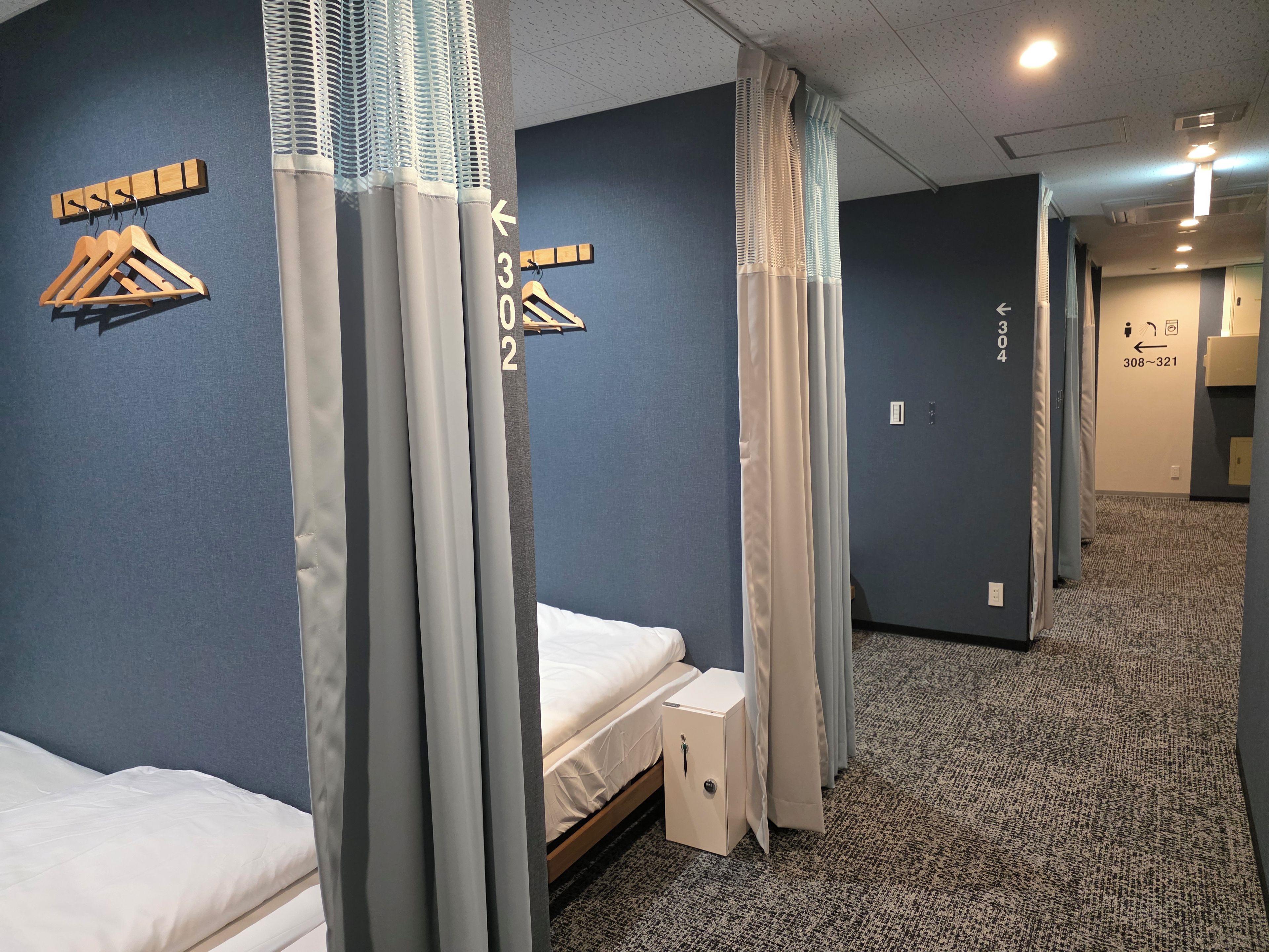 Une chambre d’hôtel avec un lit, une table de chevet et une armoire. Les fenêtres sont dotées de rideaux et les murs sont peints en bleu.