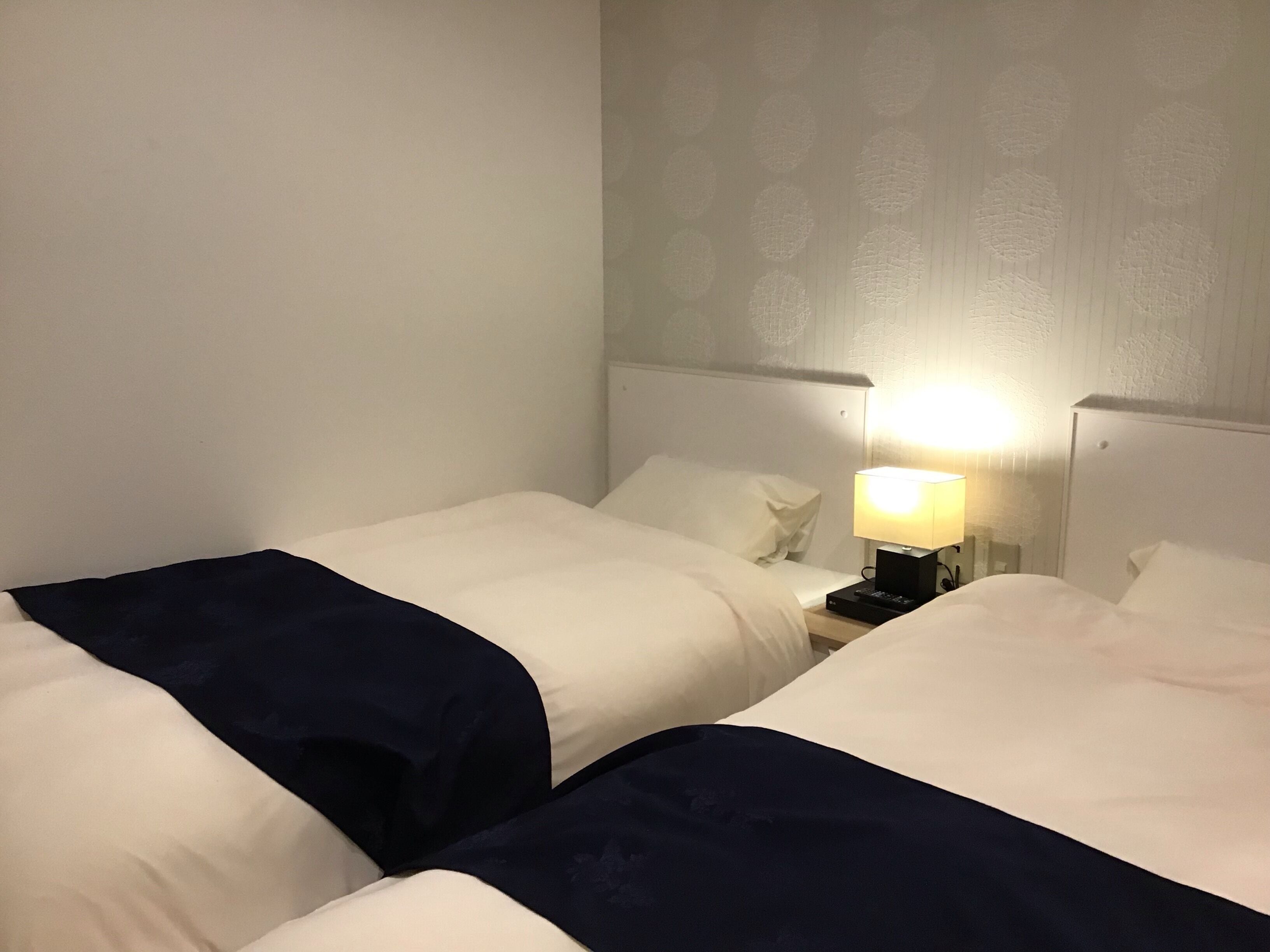 A hotel room with two beds, a nightstand with a lamp, and a patterned wall.