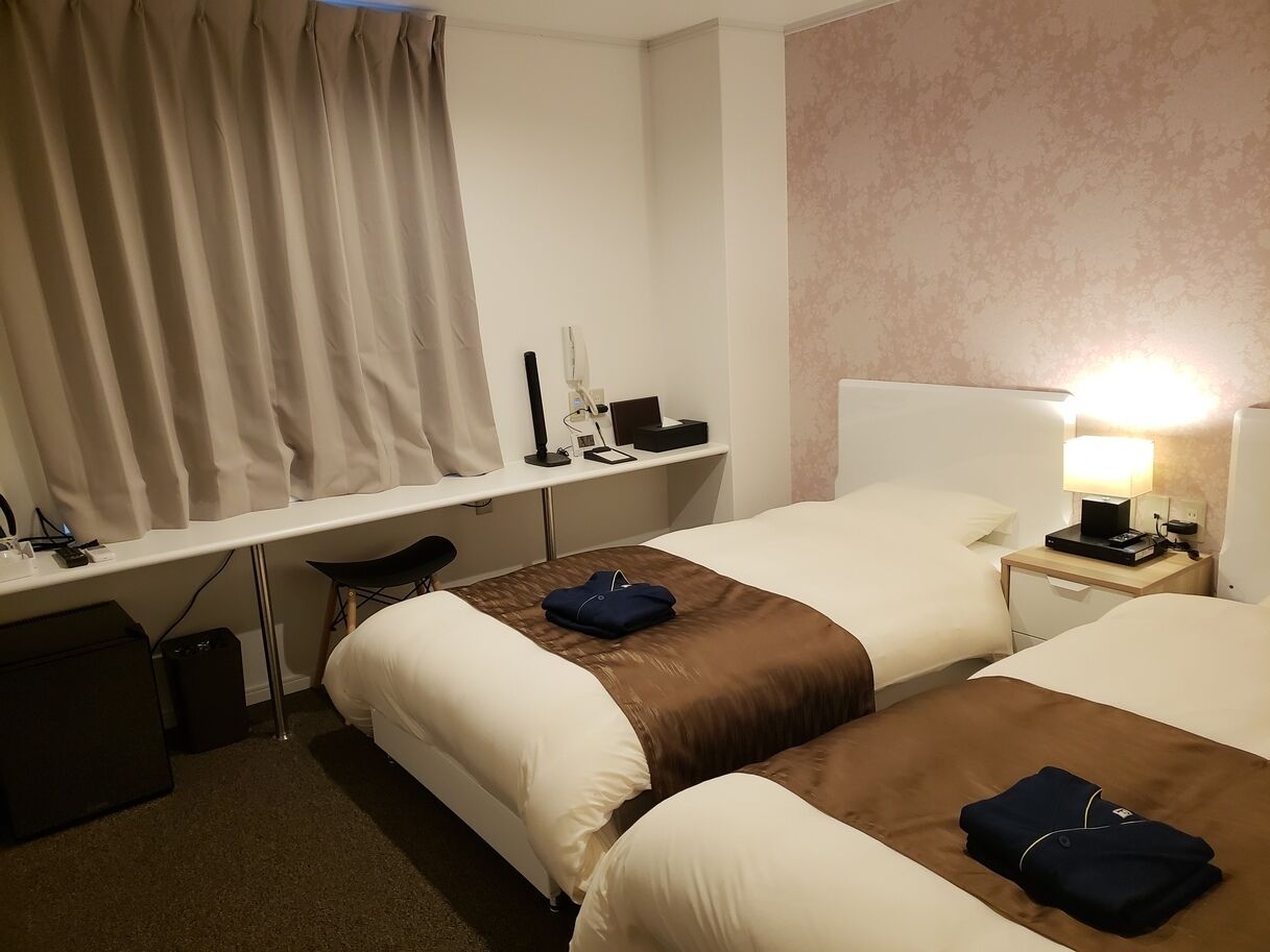 A hotel room with two beds, a desk, a chair, a lamp, and a suitcase.