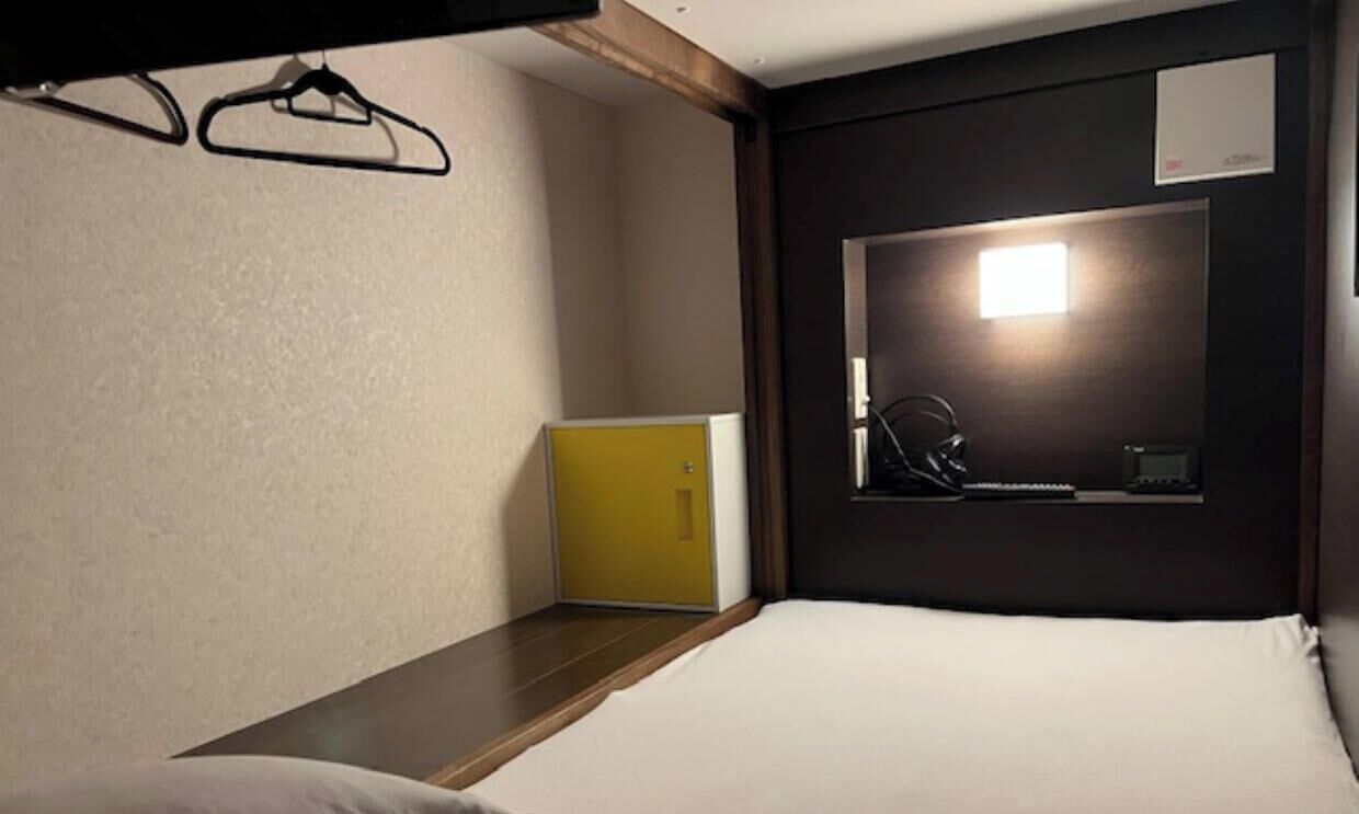 A single bed with a headboard, a bedside table, a mirror, a small yellow cabinet, and a wall-mounted light fixture.