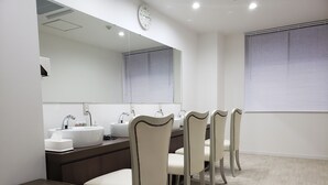 A modern bathroom with two sinks, a mirror, and a seating area with four chairs. - Hotel Carna A (Kumamoto)