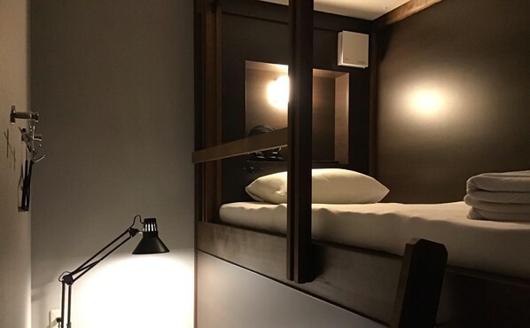 A modern hotel room with a single bed, a bedside lamp, and a mirror reflecting the room's interior. - Hotel Carna A (Kumamoto)