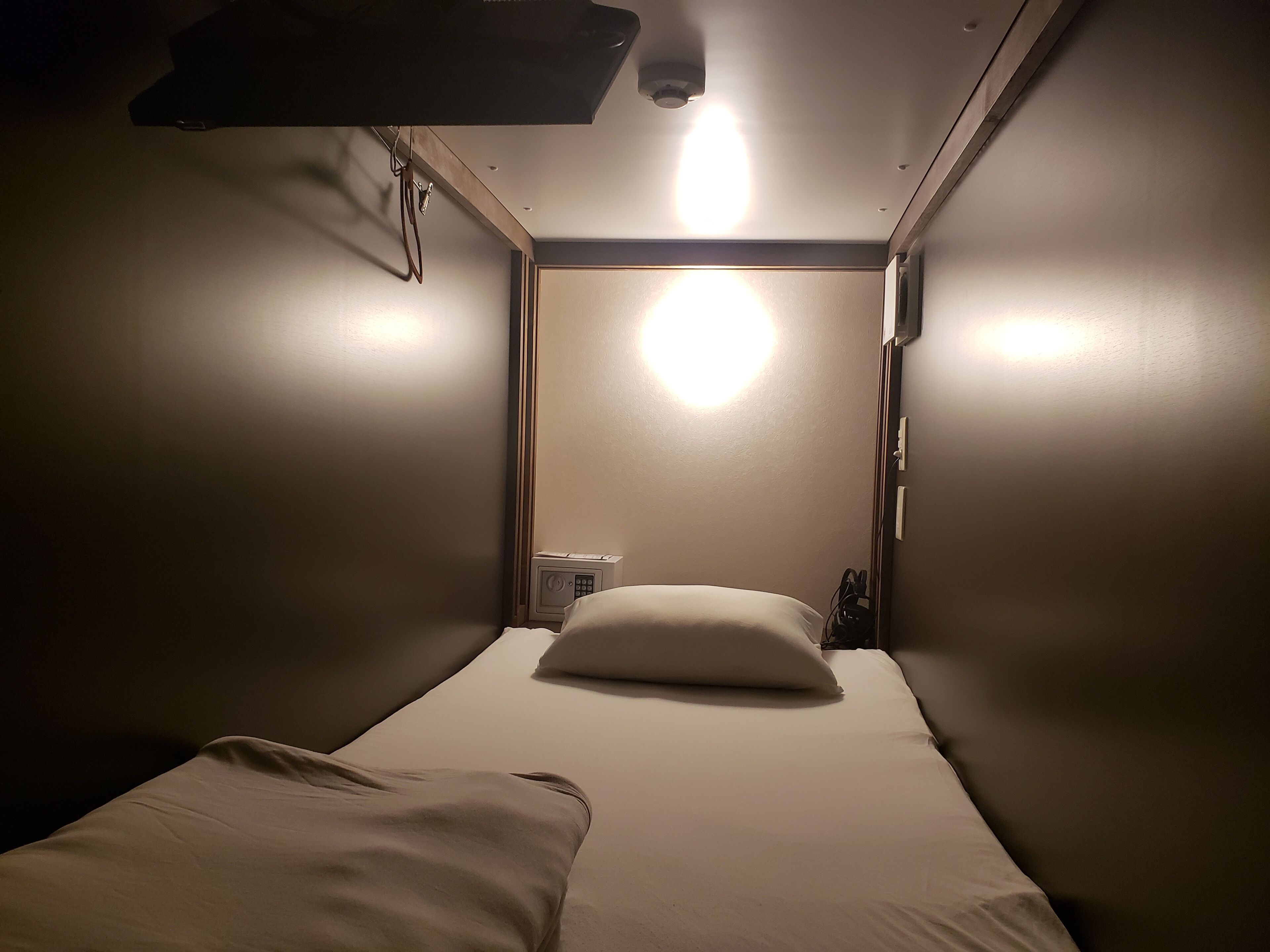 Et lille, svagt oplyst rum med to senge, en enkelt loftlampe og et lille natbord med stikkontakt.