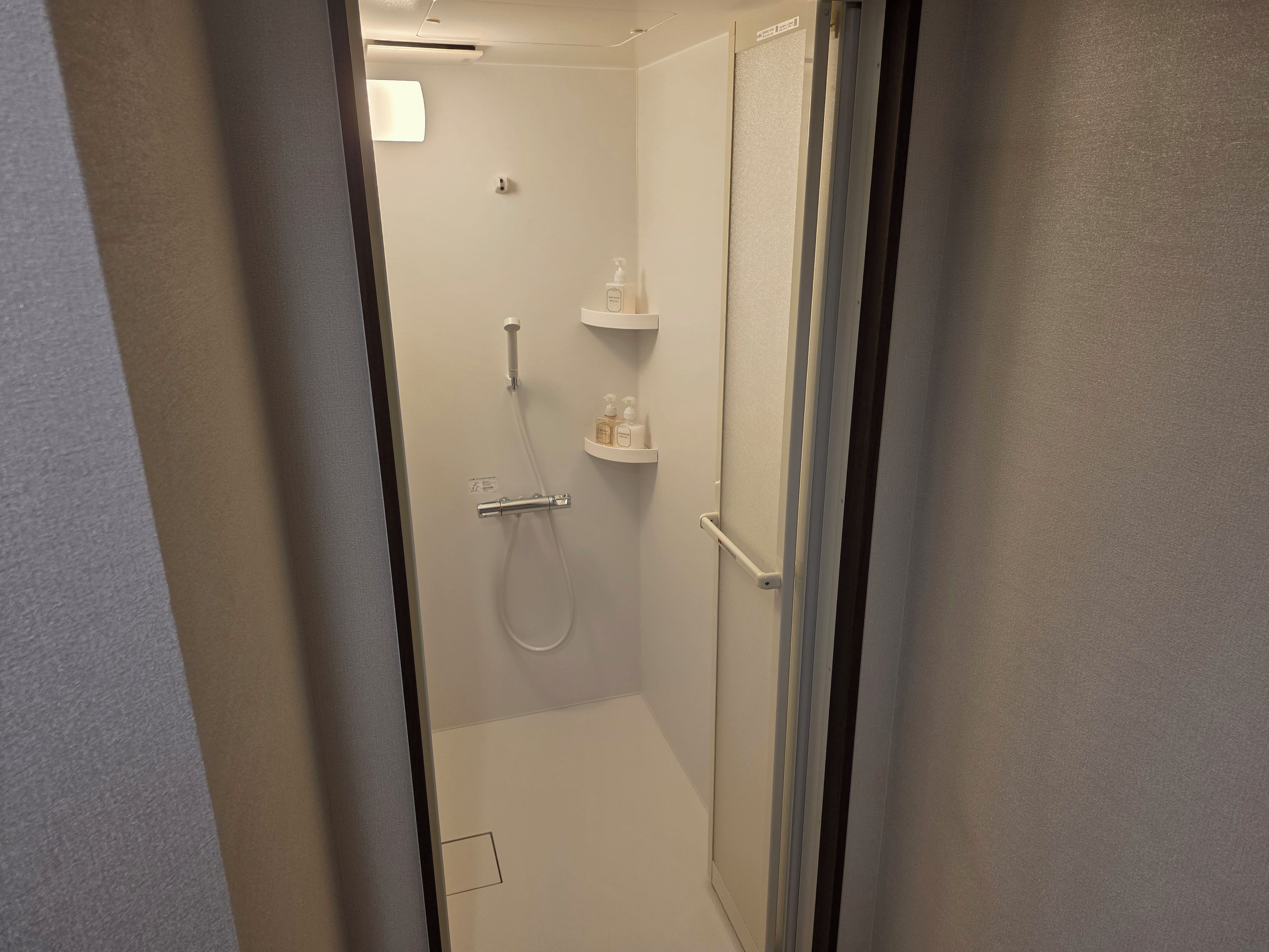 Een kleine, afgesloten douchecel met een handdouche en een handmengkraan.