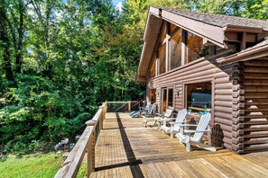 Een houten blokhut met een terras, buitenmeubels en uitzicht op het bos.