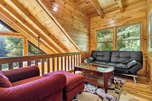 L’intérieur d’un chalet en bois, avec un plafond mansardé, un canapé en cuir noir, un fauteuil rouge et une table basse avec un plateau en verre.