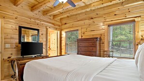 Une chambre dans une cabane en bois, comprenant un lit, une commode, un téléviseur et une fenêtre avec des stores.