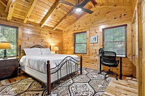 Une chambre dans une cabane en bois, comprenant un lit, un bureau, une chaise et deux fenêtres équipées de stores.