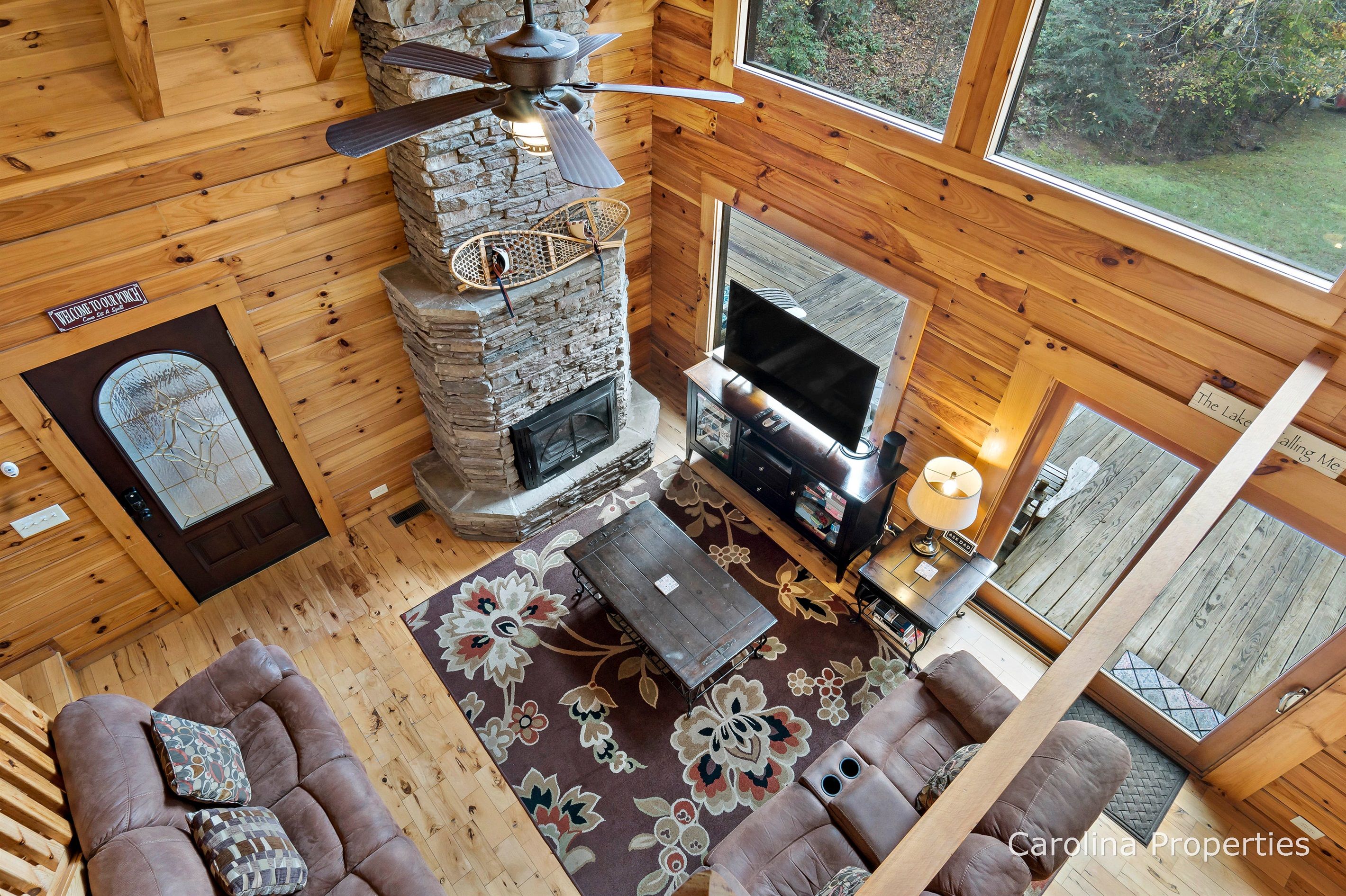 A cozy cabin interior with a stone fireplace, a television, and a large window offering a view of the outdoors.