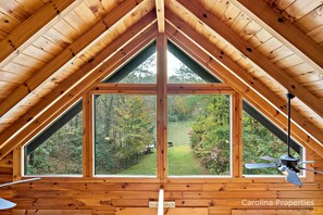 Une pièce mansardée en bois, dotée d’une grande fenêtre donnant sur une zone boisée.
