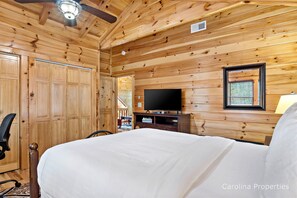 Une chambre à coucher aux murs lambrissés, équipée d’un lit, d’une télévision et d’un ventilateur de plafond.