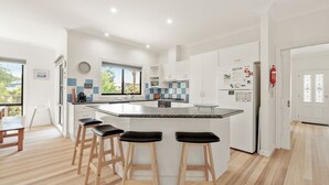 Una cucina moderna con una grande isola, sgabelli in legno, pensili bianchi e vista dalla finestra.