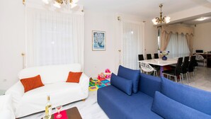 Ein Wohnzimmer mit weißem Sofa, blauem Sofa, Esstisch und Stühlen sowie einem Kronleuchter.