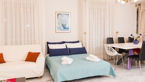 Ein Hotelzimmer mit einem Bett, einem weißen Sofa, einem Esstisch mit Stühlen und einer Kristallleuchter.
