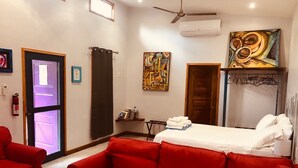 A hotel room with a red sofa, a bed with white linens, a ceiling fan, and artwork on the walls.